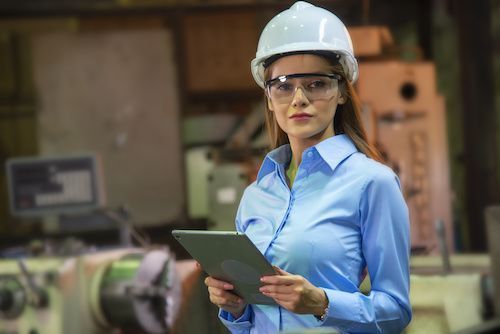 Datrice di lavoro con casco e occhiali di protezione controlla un tablet in un ambiente industriale